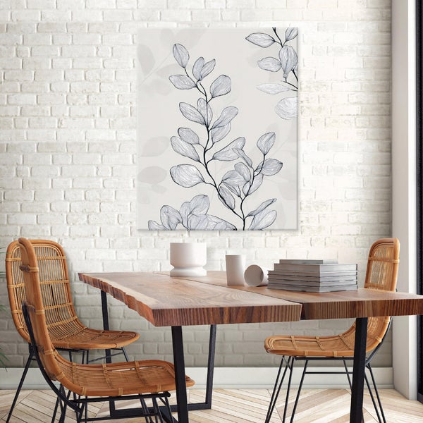 Wandbild mit stilisierter Blattzeichnung über einem Holztisch mit Rattanstühlen vor einer weißen Backsteinwand.