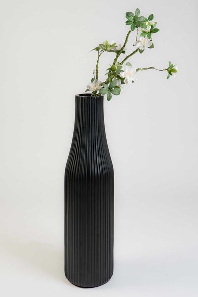 Schlanke schwarze Dekovase mit vertikalen Rillen und weißen Kunstblumen.