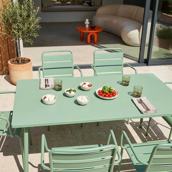 Moderne salbeigrüne Garten-Essgruppe aus Metall auf einer Terrasse mit Olivenbaum, bestehend aus einem Tisch und Stühlen mit Armlehnen.