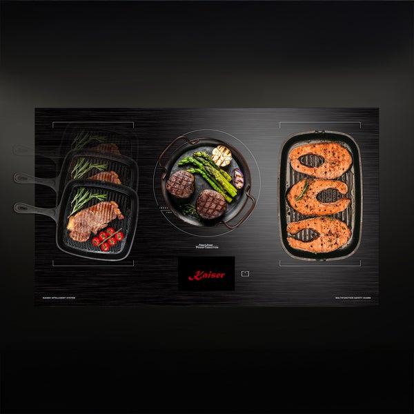Kaiser Induktionskochfeld mit integrierten Pfannen, Grillfleisch und Fischgerichten auf der Glaskeramikoberfläche.