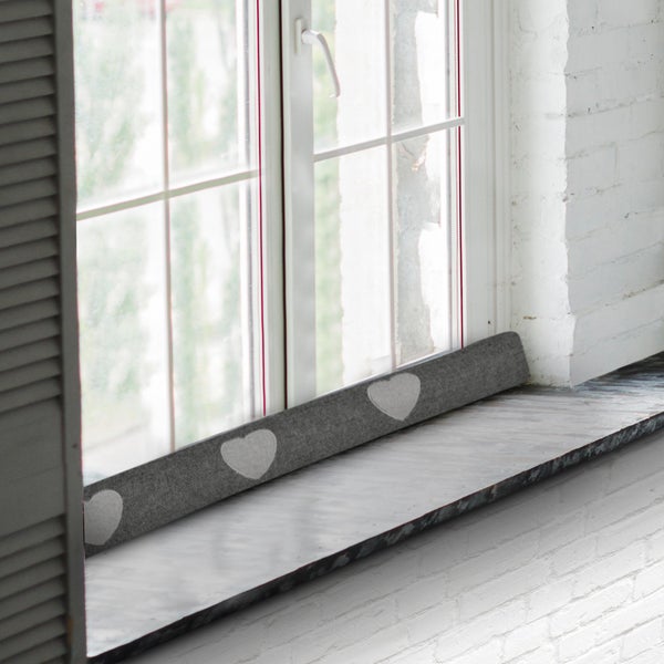Zugluftstopper mit Herzmotiven am Fensterbrett.
