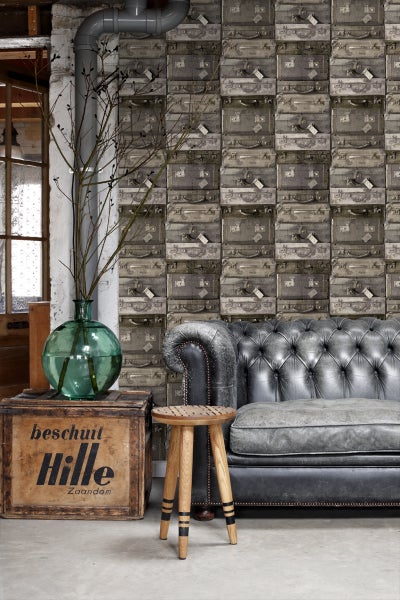 Wohnraum mit Koffertapete, Chesterfield Sofa, Holzhocker und dekorativer Vase