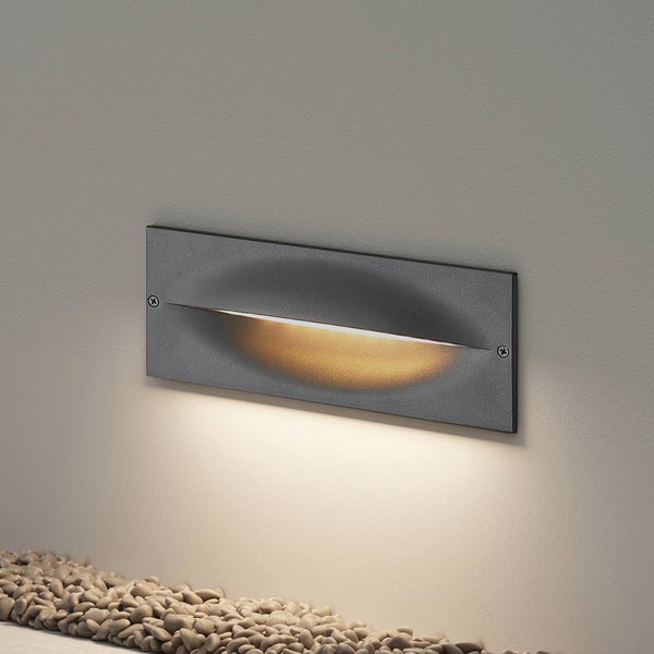 Rechteckige Außenwandleuchte in Anthrazit mit Lichtaustritt nach unten, montiert an einer Wand über Kies.