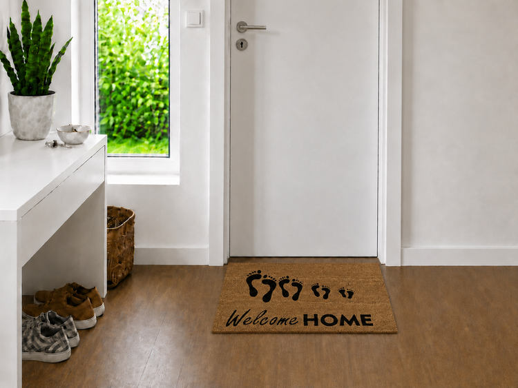 Kokos-Fußmatte mit dem Schriftzug Welcome Home und Fußabdrücken vor einer weißen Zimmertür in einem hellen, modernen Flur.