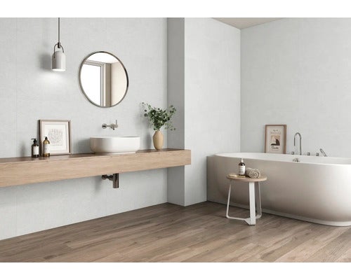 Helles Badezimmer mit Holzfußboden, Waschtisch, Spiegel und Badewanne.