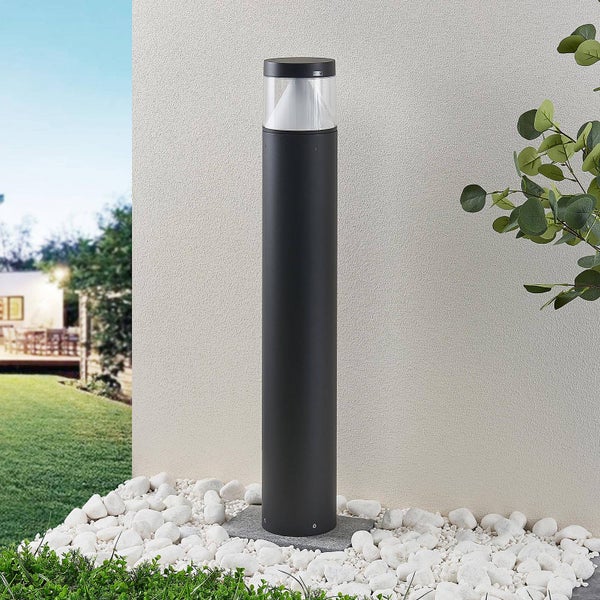 Zylindrische Außenstehleuchte in Anthrazit mit klarem Glas und konischem Reflektor, stehend in einem Bett aus weißen Kieselsteinen.