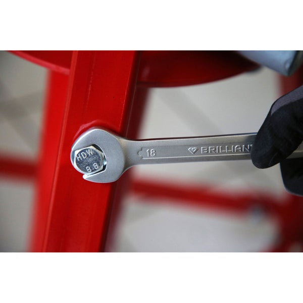 Ein Schraubenschlüssel der Größe 18 zieht eine Schraube an einem roten Metallrahmen fest.