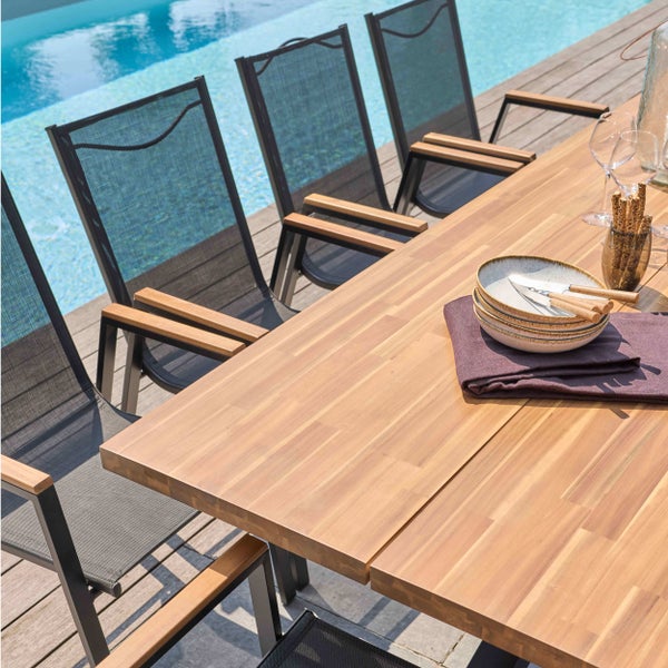 Gartentisch aus Holz mit Gartenstühlen aus Metall und Textilene auf einer Holzterrasse neben einem Pool.