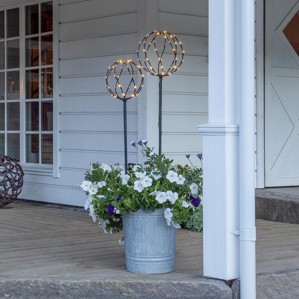 Dekorative Gartenszene mit beleuchteten Metallkugeln und einem Zinkeimer voller Blumen