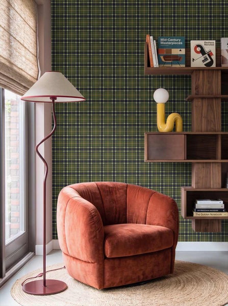 Vliestapete mit Karomuster an einer Wand in einem modern gestalteten Wohnzimmer mit Samtsessel, Holzregal und Stehlampe.