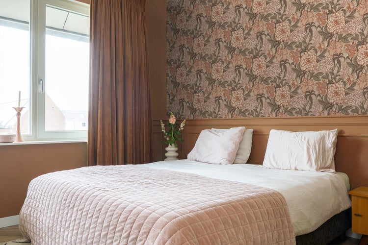 Schlafzimmer mit Doppelbett, floraler Tapete und Vorhängen