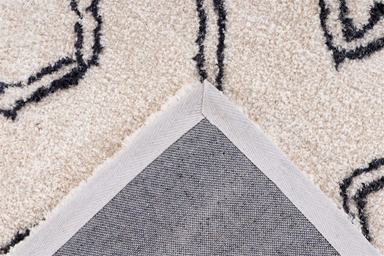 Nahaufnahme eines Teppichs mit dunklem Muster, die umgeschlagene Ecke zeigt die Rückseite und die Kantenverarbeitung.