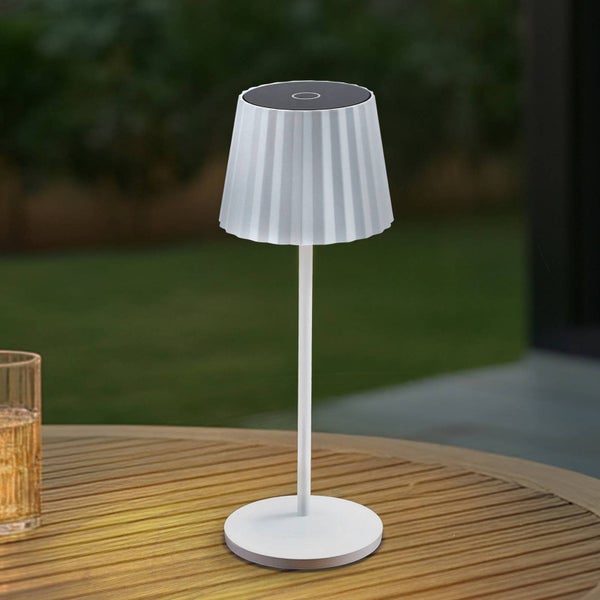 Moderne, tragbare Solar-Tischleuchte mit gefaltetem Schirm auf einem runden Holztisch im Außenbereich.