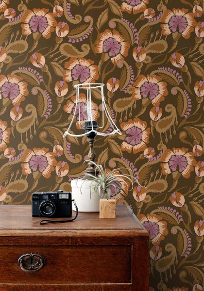 Vliestapete mit großem floralem Paisleymuster in einer Raumszene mit Holzkommode, Kamera, Lampengestell und kleiner Pflanze.