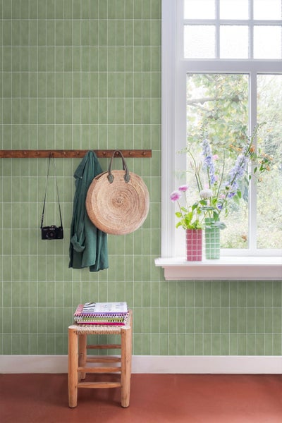 Flur mit Wandfliesen im Hochformat an einer Wand, daneben ein Fenster, eine Garderobe mit Tasche und Jacke sowie ein Hocker mit Zeitschriften.