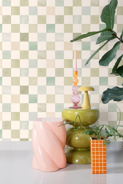 Raumansicht mit Schachbrettmuster Tapete und dekorativen Elementen wie Hocker, Kerzen und Pflanzen.