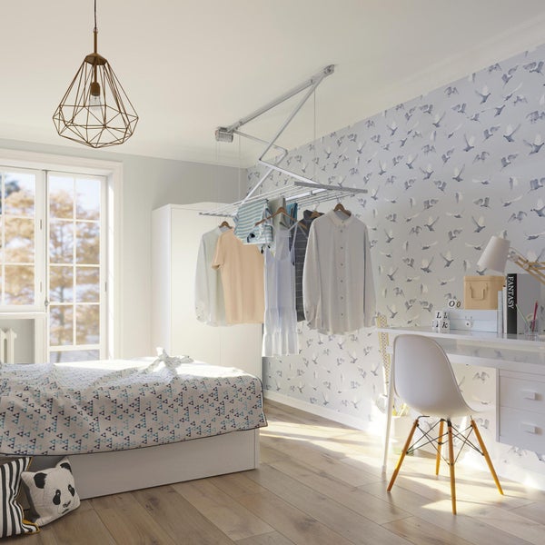 Helles Zimmer mit Deckenwäscheständer, Bett, Schreibtisch und Stuhl.