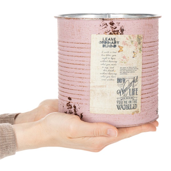 Dekorativer Übertopf aus Metall in Rosa mit Vintage-Etikett, gehalten von zwei Händen zur Veranschaulichung der Größe.