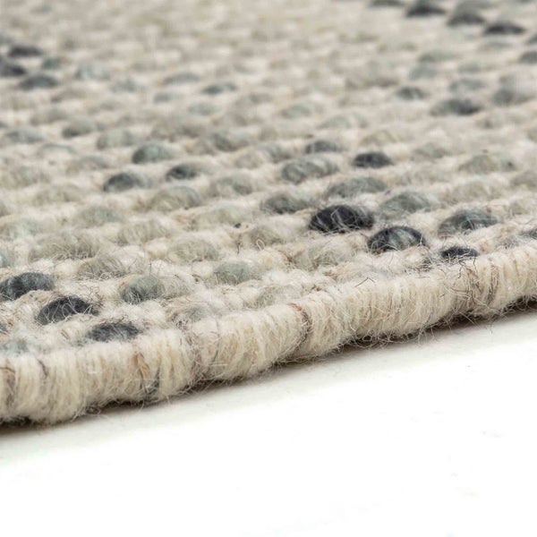 Nahaufnahme eines strukturierten Wollteppichs mit grauem und cremefarbenem Noppenmuster, die Webart und Kante zeigt.