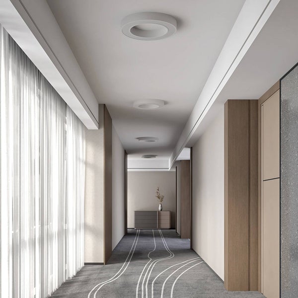 Moderner, heller Flur mit runden weißen Deckenleuchten, einer großen Fensterfront mit Vorhängen und gemustertem grauem Teppich.