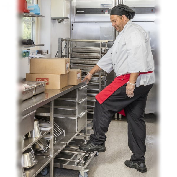 Ein Koch steht auf einer fahrbaren Trittstufe aus Edelstahl in einer gewerblichen Küche.