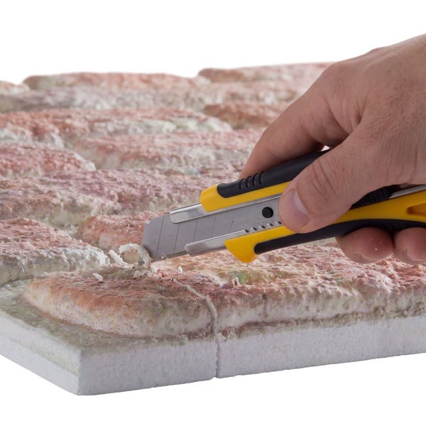 Hand schneidet mit einem Cuttermesser ein Dämmplattenelement mit Ziegelsteinoptik zu.