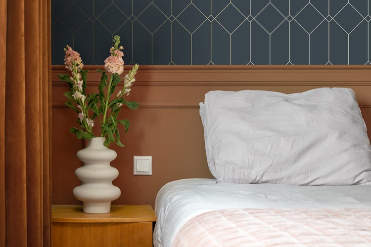 Schlafzimmer mit Bett, Nachttisch, Vase mit Blumen und geometrischer Tapete