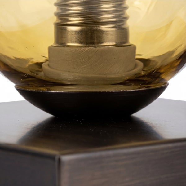 Nahaufnahme einer Tischleuchte mit dunklem Metallsockel, bernsteinfarbenem Glas und E27 Fassung.