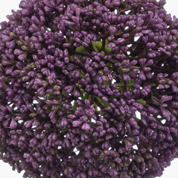 Detailaufnahme einer künstlichen Skabiose mit rosa-weißen Blütenblättern und grünen gezackten Blättern.