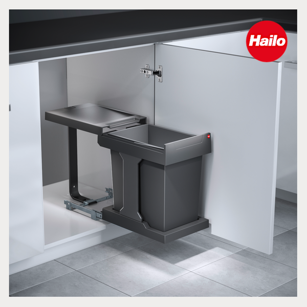 Ausziehbarer Einbaumülleimer mit einem grauen Behälter in einem weißen Küchenunterschrank. Hailo Logo.