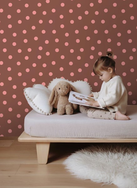 Vlies-Fototapete mit Pünktchenmuster im Kinderzimmer, Kind liest ein Buch auf einem Holzbett mit Stoffhase und Kissen.
