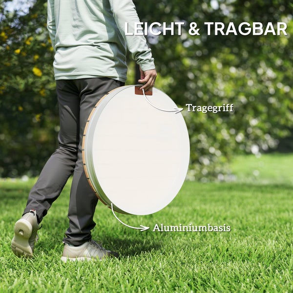 Person trägt eine runde tragbare Leuchte mit Aluminiumbasis und Griff im Garten. Text Leicht und tragbar, Tragegriff, Aluminiumbasis.