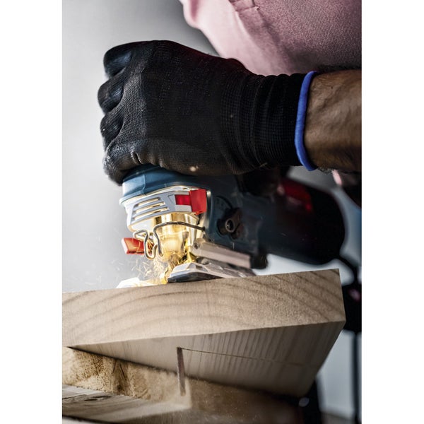 Nahaufnahme einer Stichsäge beim Schneiden eines Holzstücks, mit einem Arbeiter der Handschuhe trägt