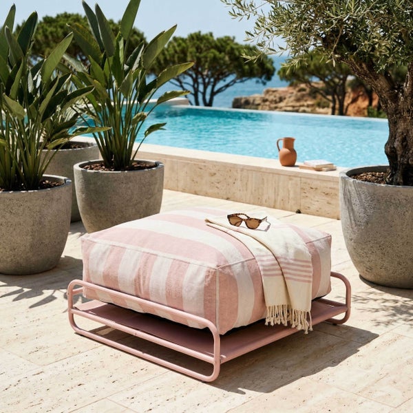 Quadratischer Outdoor-Sitzhocker mit Metallgestell und gestreiftem Kissen auf einer Terrasse am Pool, umgeben von Pflanzen in Betontöpfen.