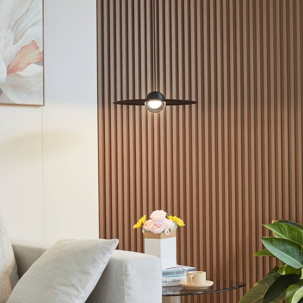 Moderne schwarze Pendelleuchte mit flachem Schirm vor einer Wand aus Holzlamellen in einem hellen Wohnzimmer.