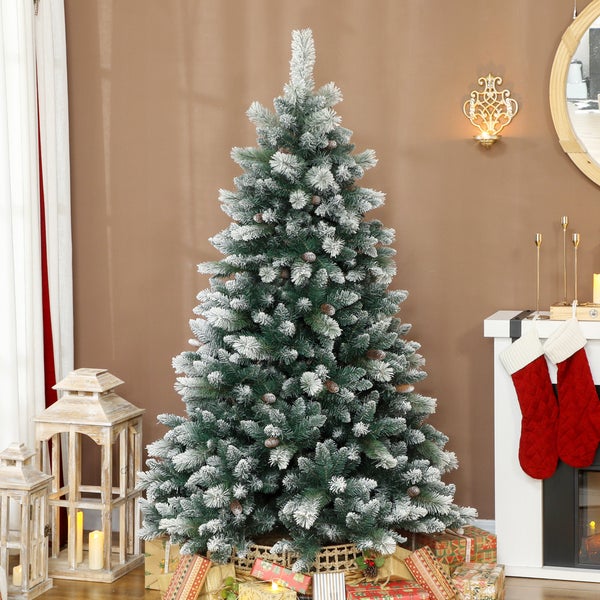 Künstlicher Weihnachtsbaum mit verschneiten Zweigen und Tannenzapfen in einem hellen Raum mit Kamin, Laternen und Geschenken.