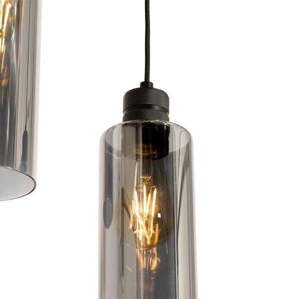 Detailansicht einer Pendelleuchte mit zylindrischem Rauchglasschirm, schwarzer Metallfassung und leuchtendem Filament-LED-Leuchtmittel.