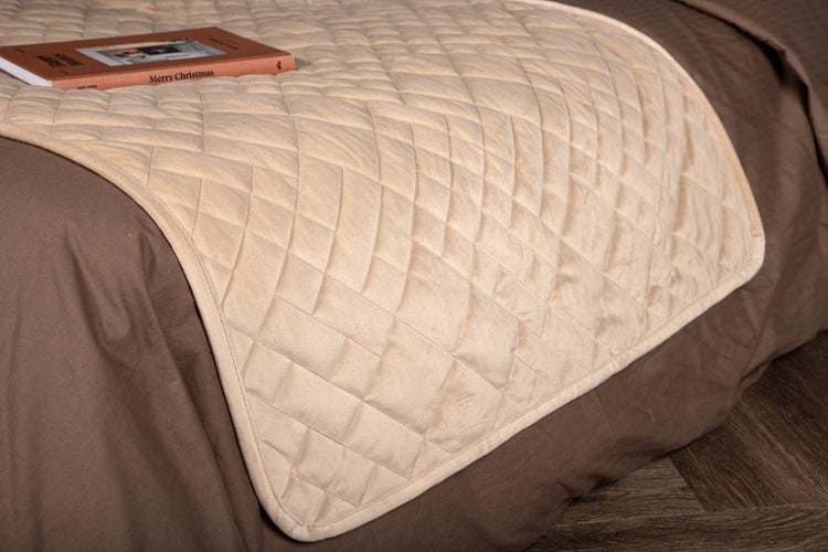 Gesteppter Bettläufer mit Rautenmuster aus weichem Material auf einem Bett in einem ordentlichen Schlafzimmer.