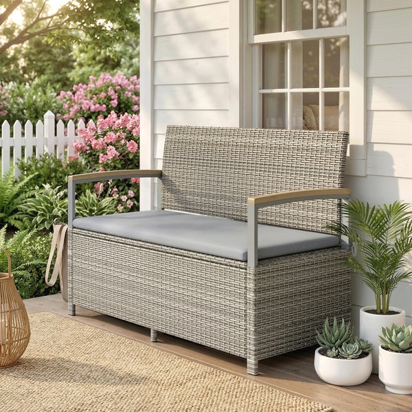 Gartenbank mit Truhenfunktion aus Polyrattan mit grauem Sitzkissen und Armlehnen aus Holz vor einer hellen Hauswand auf einer Terrasse.