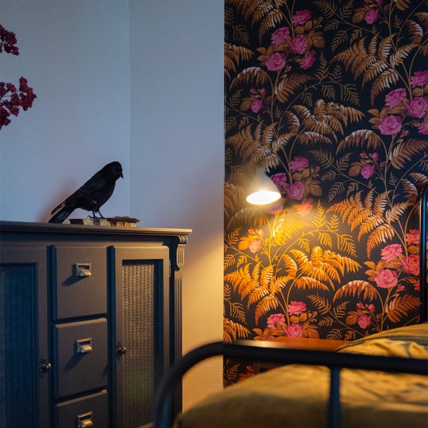 Schlafzimmer mit Kommode, Rabenfigur und geblümter Tapete