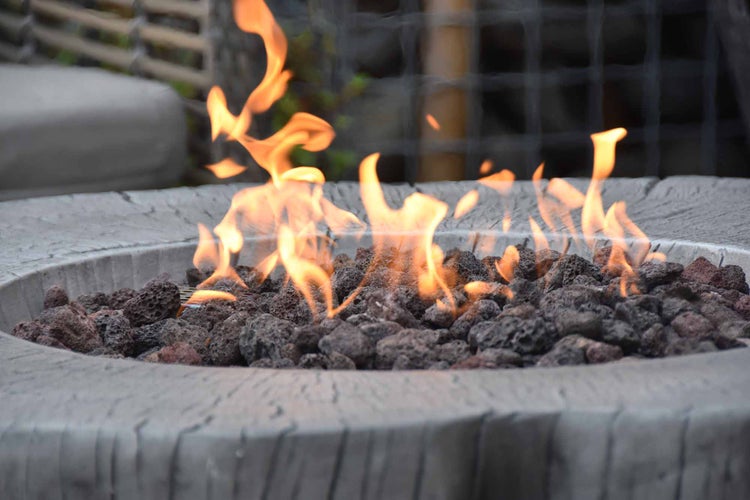 Gas-Feuerstelle mit Lavasteinen und brennenden Flammen in Steinoptik für den Außenbereich.