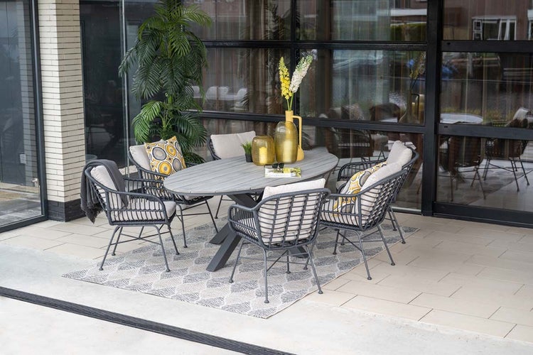 Modernes Gartenmöbel-Set auf einer hellen Terrasse mit ovalem Tisch in Holzoptik, fünf Seilgeflecht-Sesseln, Sitzkissen und einem Outdoorteppich.