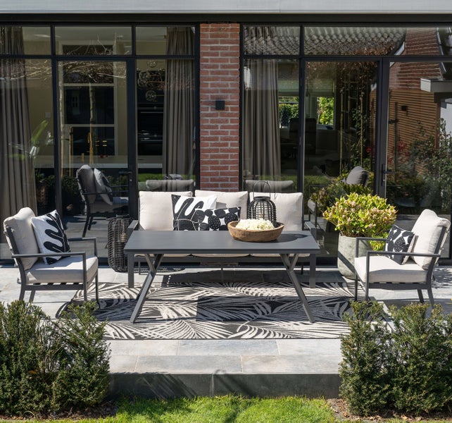 Modernes Garten-Lounge-Set auf einer Steinterrasse, bestehend aus einem Dreisitzer-Sofa, zwei Sesseln und einem rechteckigen Loungetisch.