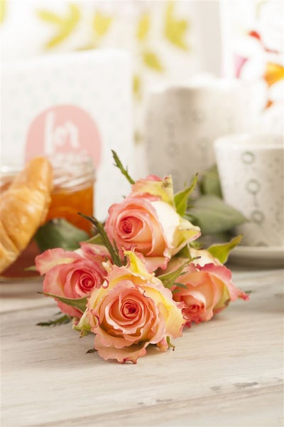 Stillleben mit Rosen, Marmelade, Croissant und Tassen auf einem Tisch.