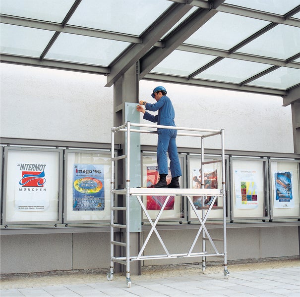 Mann auf Rollgerüst bei Montagearbeiten an einer Wand mit Plakaten