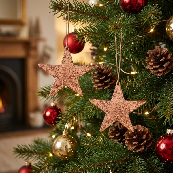 Zwei sternförmige Weihnachtsanhänger mit strukturierter Oberfläche hängend am Tannenbaum mit Kugeln und Zapfen