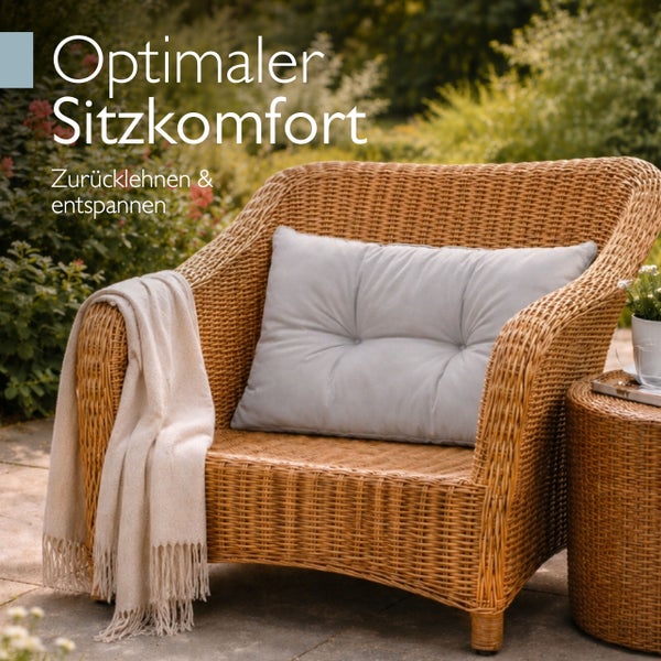 Gartensessel aus Polyrattan mit Sitzkissen und Decke auf einer Terrasse vor Gartenkulisse