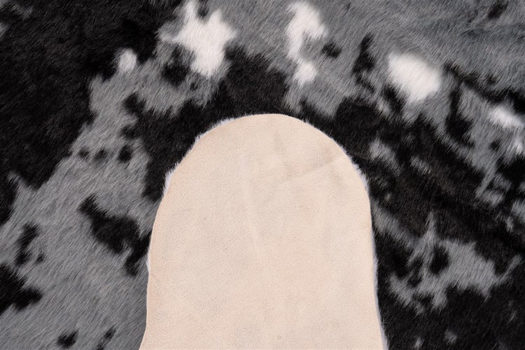 Nahaufnahme eines Kuhfellteppichs mit schwarz-grau gemusterter Oberseite und heller Lederunterseite.