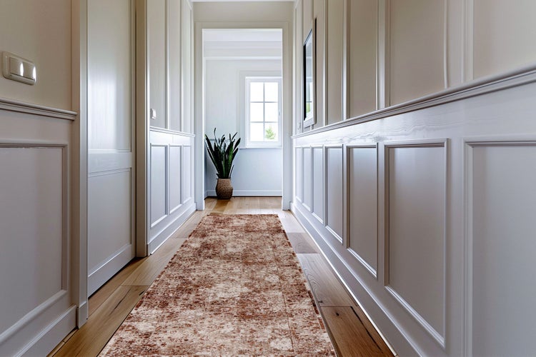 Ein heller, klassischer Flur mit Wandverkleidungen im Kassettenstil und einem rustikalen Läuferteppich auf einem Holzboden.