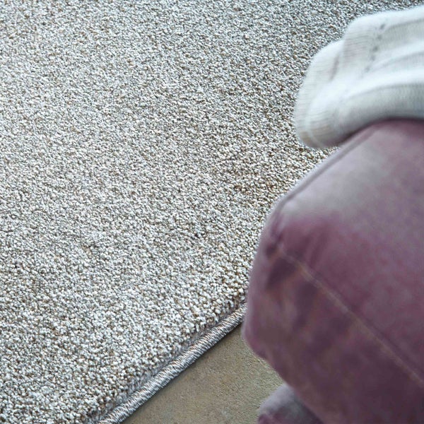 Nahaufnahme eines strukturierten Teppichs mit eingefasster Kante neben einem Polstermöbel.